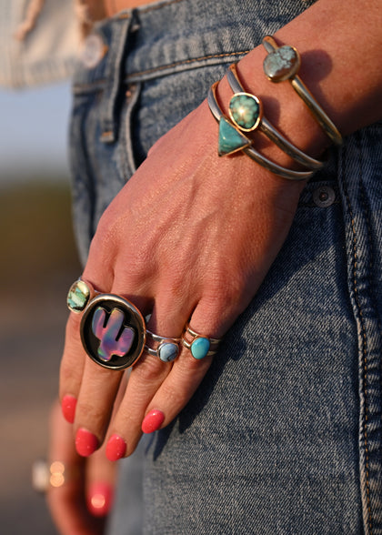 Hand with multiple rings and bracelets against a blurred natural background